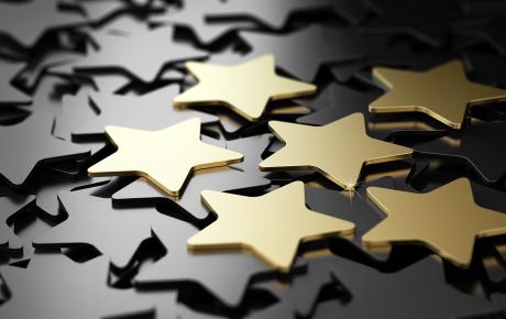 A stock image of metalic stars laid out, with 5 prominent gold ones resting on top.