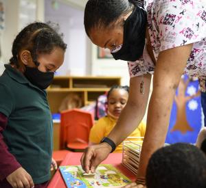 Shanikia Johnson, a three-year-olds teacher, helps Magjor Jones clean up a puzzle at Little Flowers Early Childhood and Development Center in the Sandtown-Winchester neighborhood of Baltimore, Maryland on Jan. 12, 2021. Crystal Hardy-Flowers, owner and founder of the center, died from COVID-19 complications Dec. 31. She was 55 / Photo by Matt Roth for The Washington Post via Getty Images.