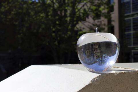A crystal apple sits on a ledge in the sunshine reflecting Lillis Hall at the University of Oregon.