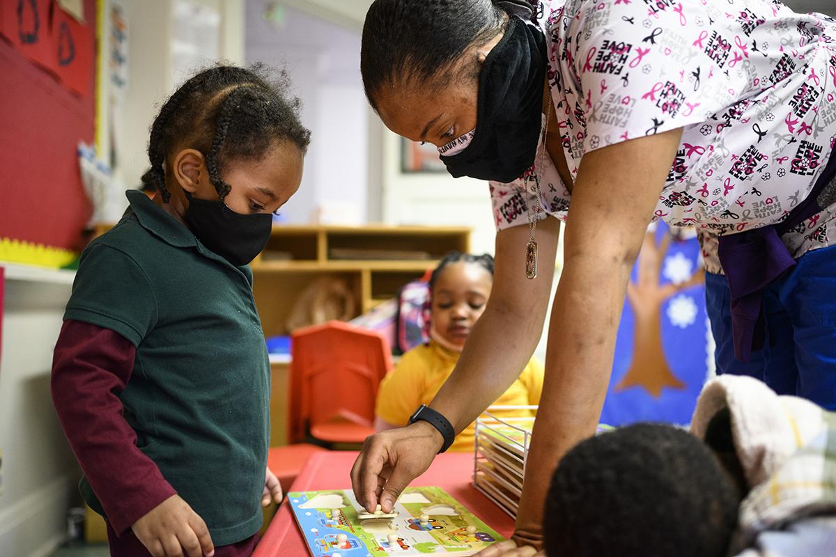 Shanikia Johnson, a three-year-olds teacher, helps Magjor Jones clean up a puzzle at Little Flowers Early Childhood and Development Center in the Sandtown-Winchester neighborhood of Baltimore, Maryland on Jan. 12, 2021. Crystal Hardy-Flowers, owner and founder of the center, died from COVID-19 complications Dec. 31. She was 55 / Photo by Matt Roth for The Washington Post via Getty Images.