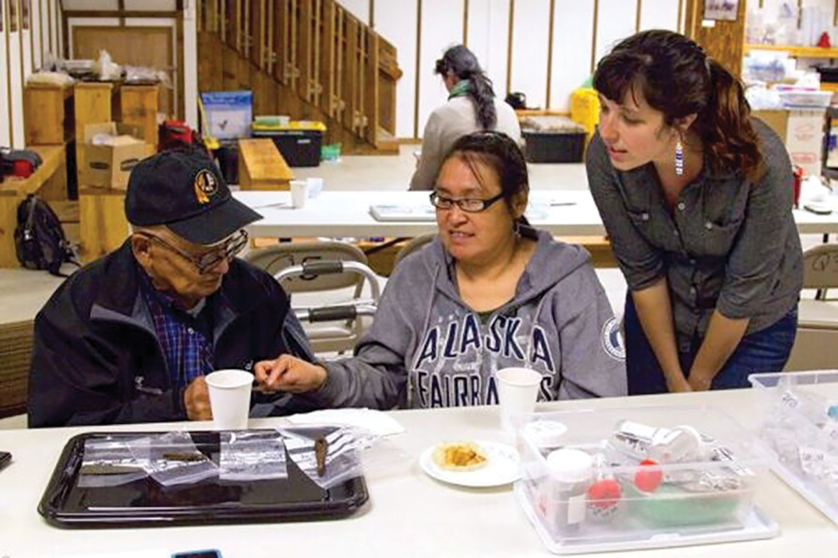 Village elder George Pleasant, Yup’ik speaker and translator Mary Church, and Anna Sloan looking at artifacts in the midst of interview research. 